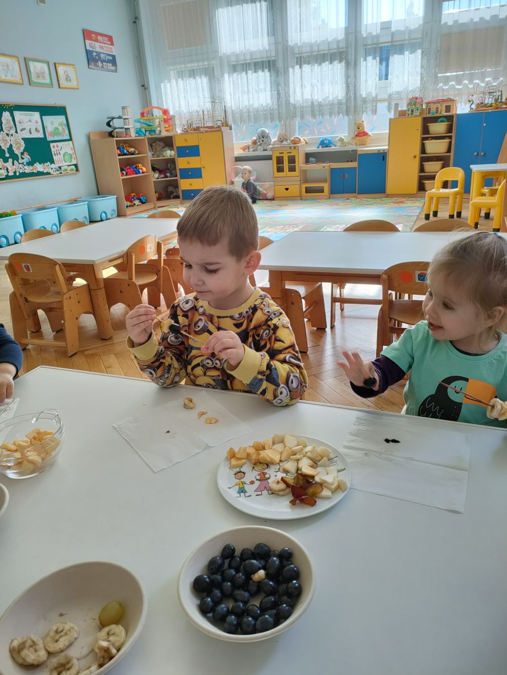 Dzieci siedzą przy stole i robią owocowe szaszłyki