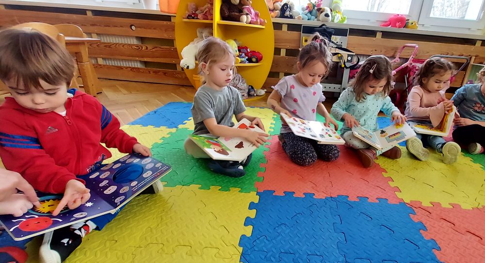 Dzieci siedzą na dywanie i oglądają książeczki