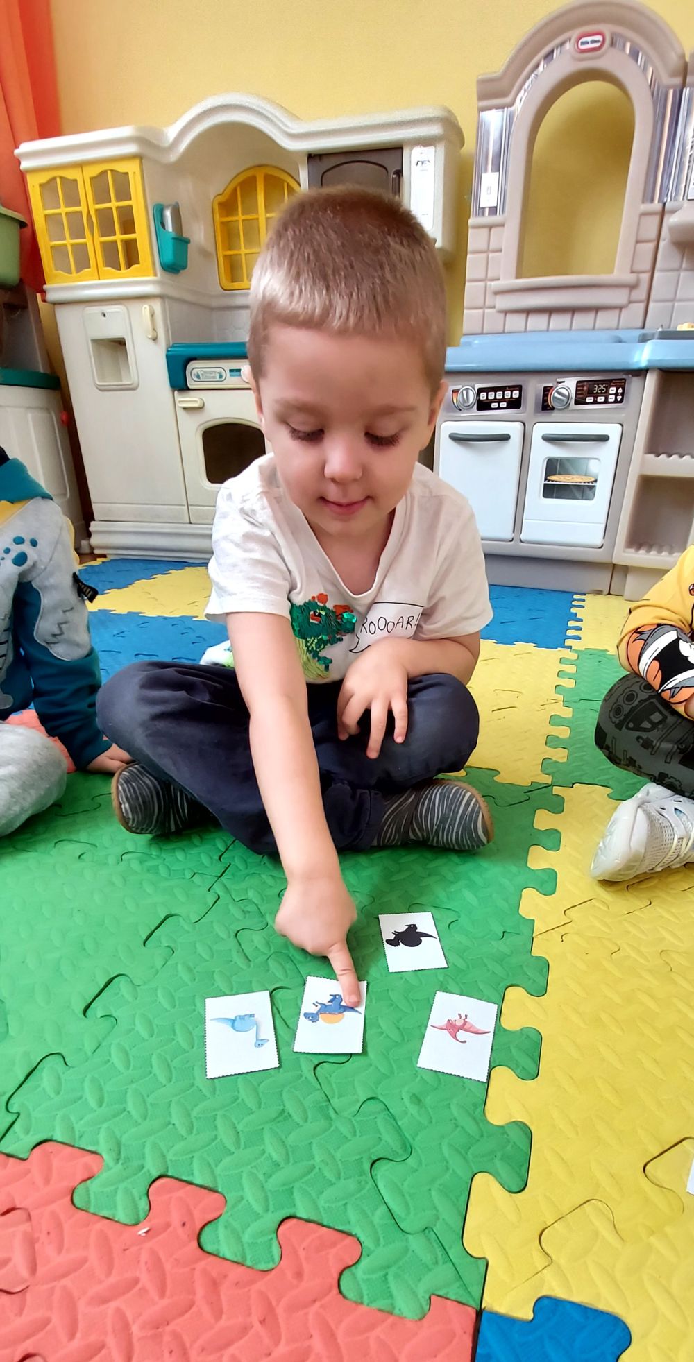 Chłopiec siedzi na dywanie i pokazuje palcem na obrazek dinozaura