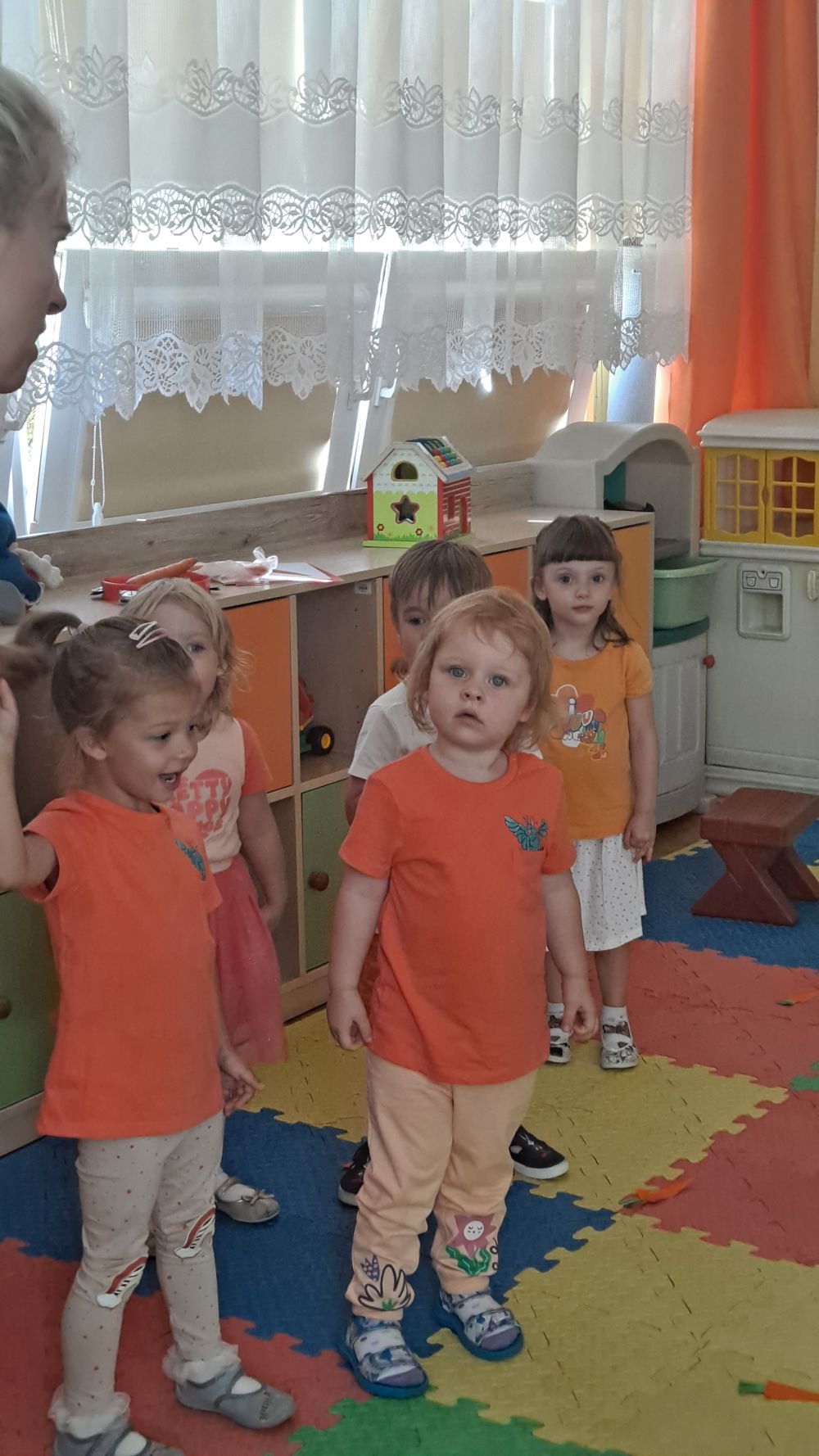 Dzieci stoją na dywanie ubrane na pomarańczowo
