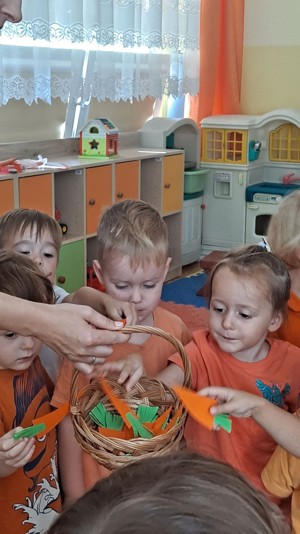 Dzieci biorą z koszyczka papierowe marchewki