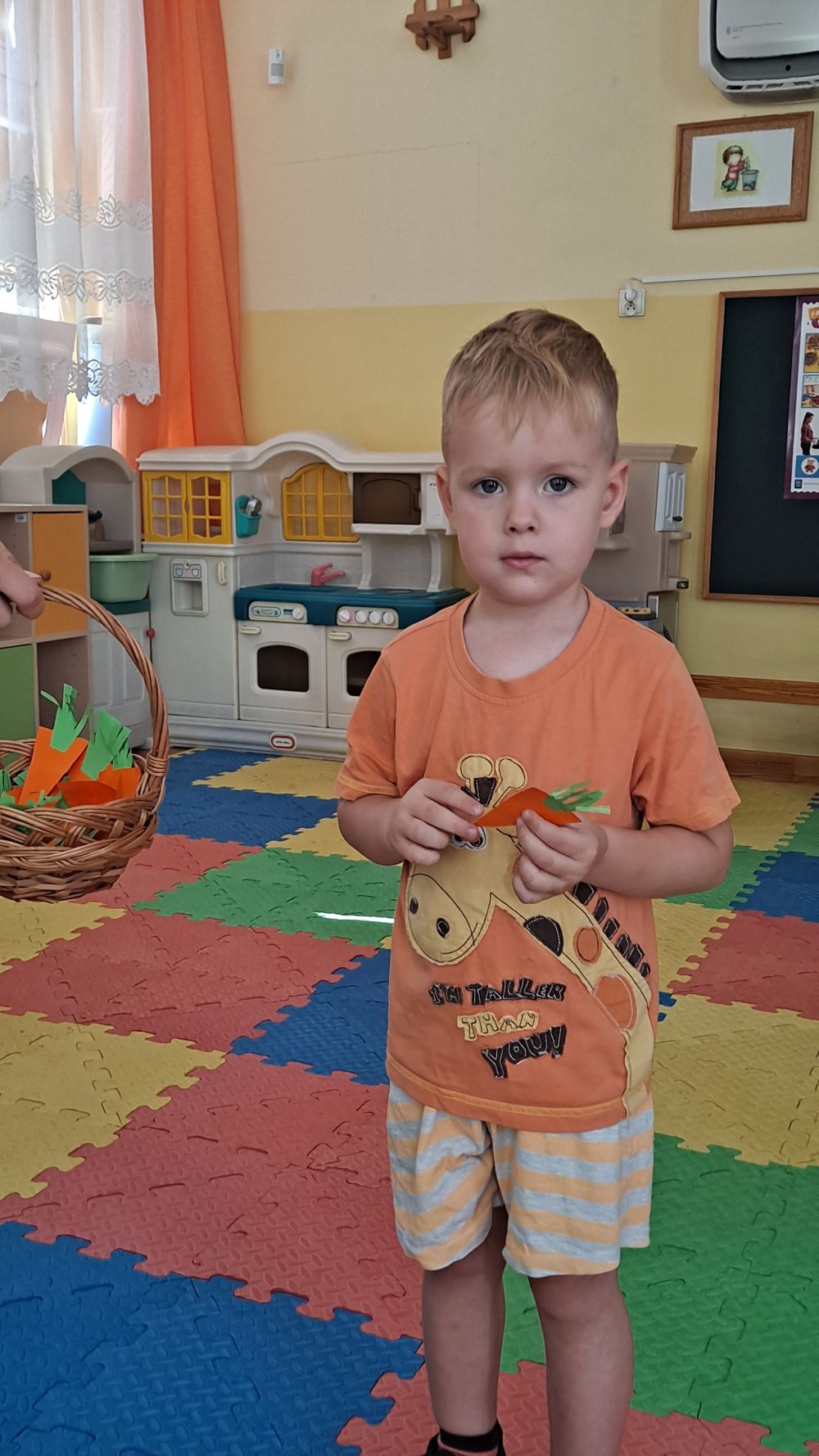 Chłopiec ubrany na pomarańczowo trzyma w ręce marchewkę z papieru