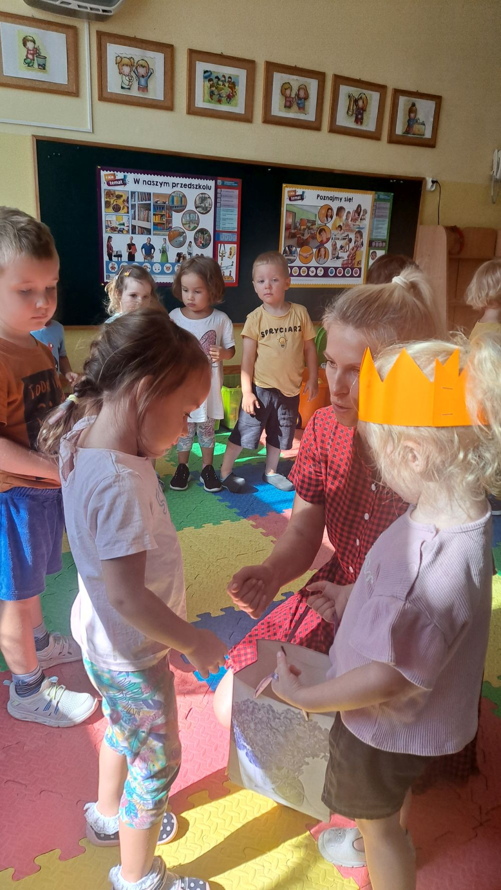Dziewczynka w koronie rozdaje cukierki dzieciom z grupy