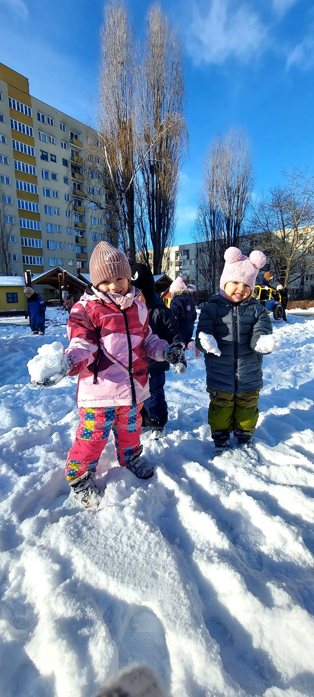 dwie dziewczynki stoją na placu zabaw i trzymają w rękach śniegowe kulki