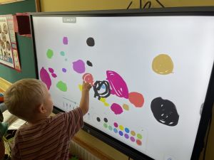 Chłopiec maluje kropkę na tablicy multimedialnej