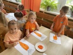 Dzieci siedzą przy stoliku i malują farbami obrazek marchewki