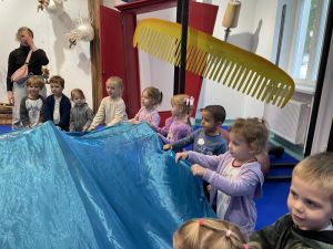 Dzieci stoją w kole i trzymają w rękach niebieski materiał