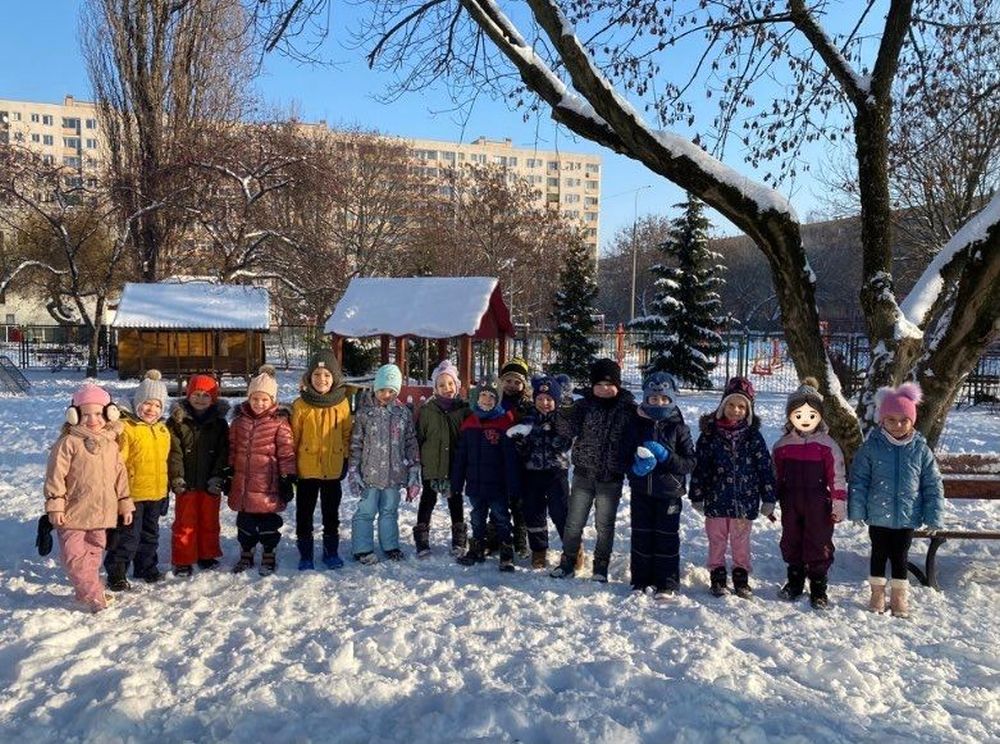 Dzieci stoją na przedszkolnym placu zabaw, zasypanym śniegiem