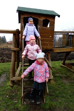 trzy dziewczynki stoją na schodkach drewnianego domku