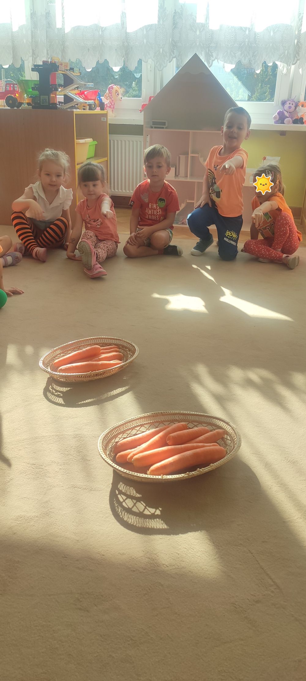 Zajęcia na dywanie, dzieci siedzą w kole, na środku leżą dwa koszyki z marchewkami