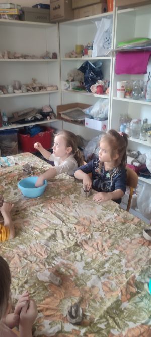 Dwie dziewczynki siedzą przy stole i lepią donniczki z gliny