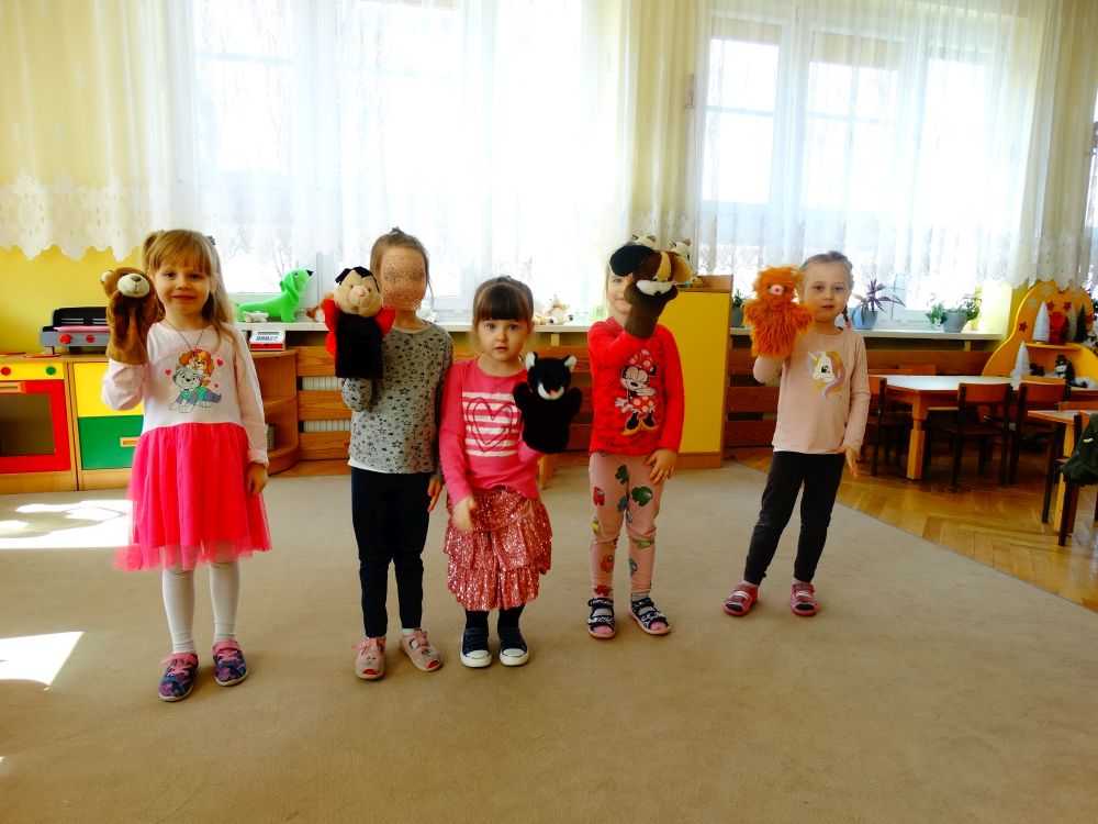 5 dziewczynek stoi w rzędzie i pokazuje rózne kukiełki