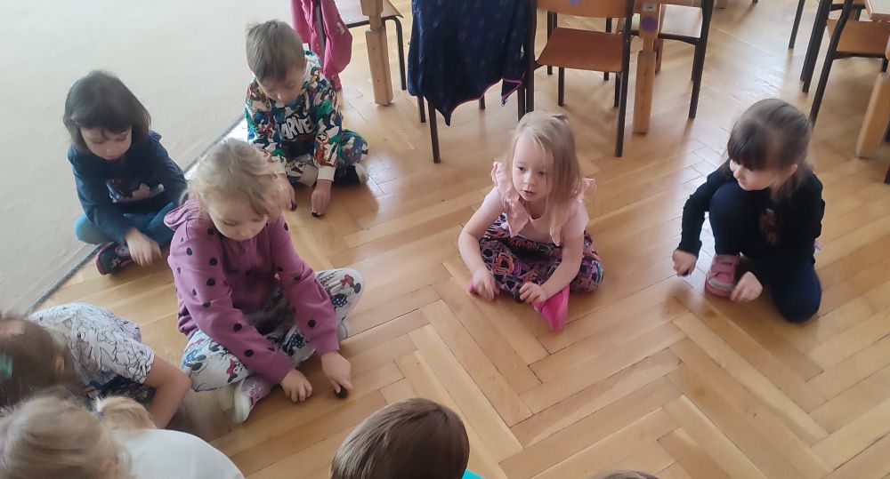 Dzieci siedzą na dywanie stukają kasztanami o podłogę