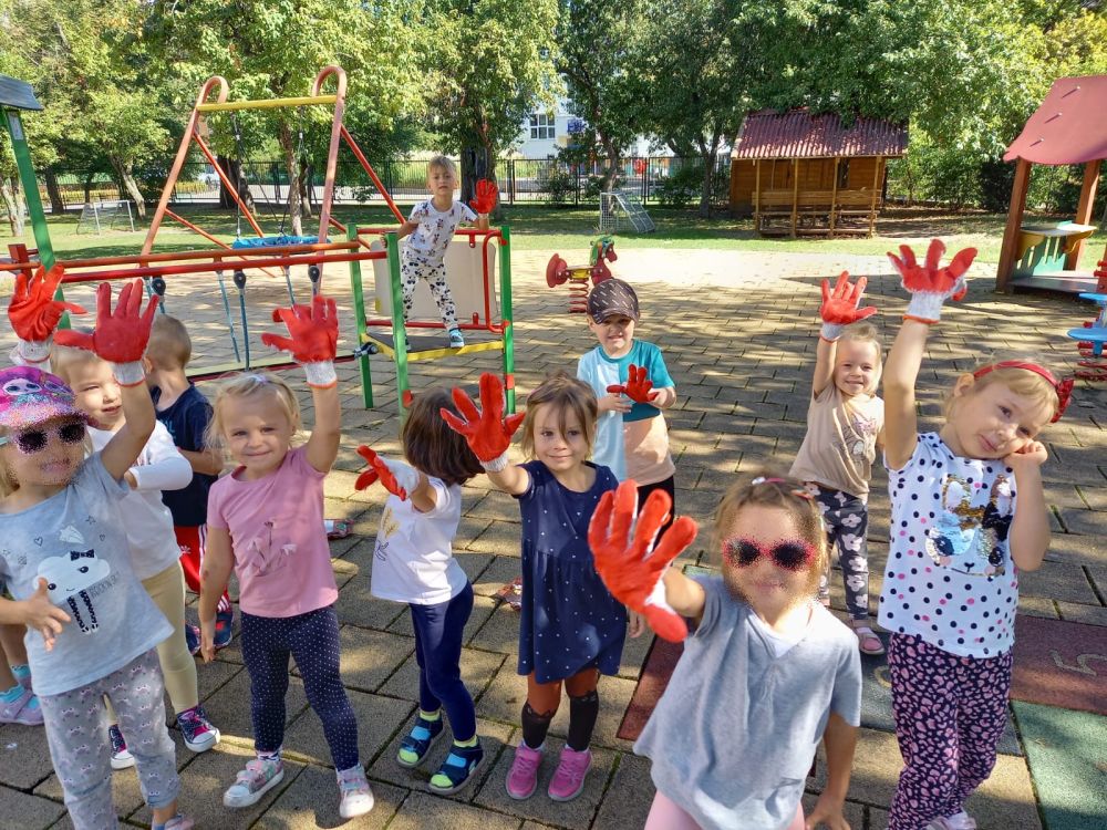 Dzieci stoją na placu zabaw i pokazują założone na ręce rękawiczki