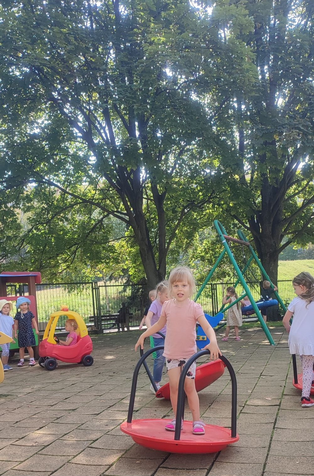 Dzieci bawią się na placu zabaw, dziewczynka stoi na platformie balansującej