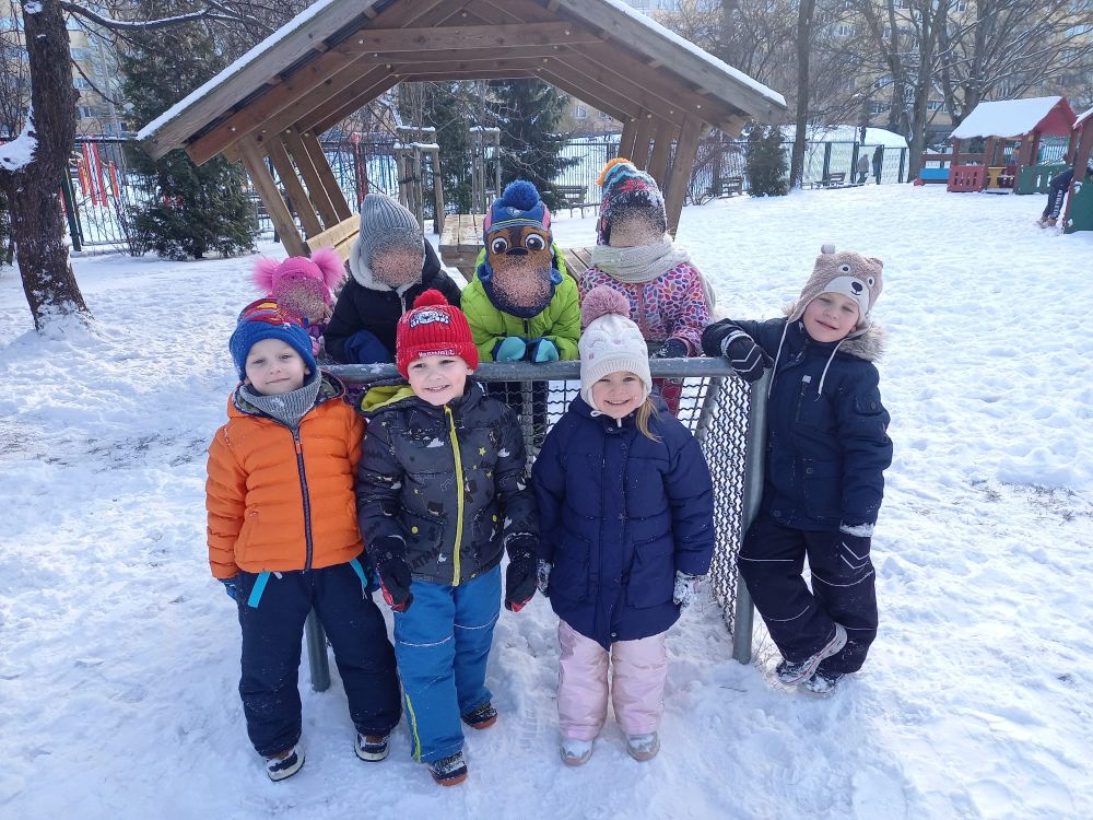 Grupka dzieci stoi w ogródku przedszkolnym zasypanym śniegiem