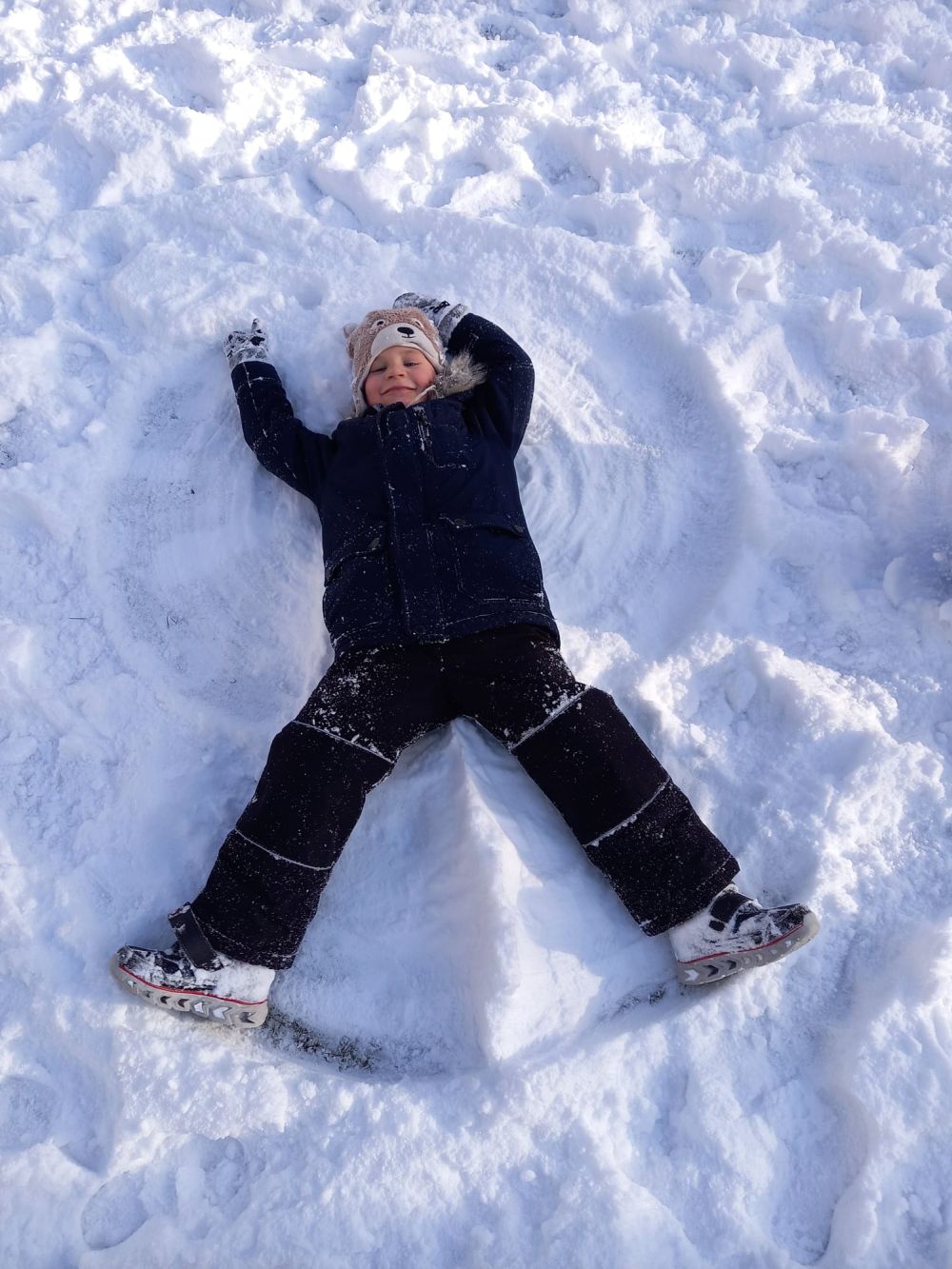 Chłopiec leży na śniegu i robi aniołka