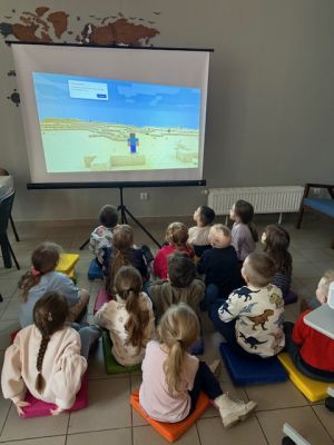 Dzieci siedzą na poduszkach i patrzą na wyświetlany obraz Minecraft