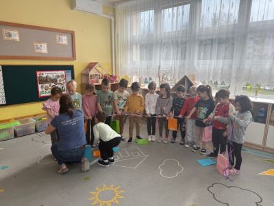 Dzieci stoją w półkolu, a mama Marysi wraz z pomocnikiem rozdają coś dzieiom