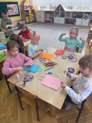 Dzieci siedzą przy stolikach i ozdabiają papierowe torebki