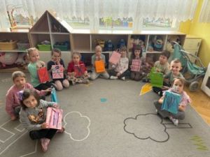 Dzieci siedzą na dywanie w półkolu i pokazują zrobione przez siebie torebki