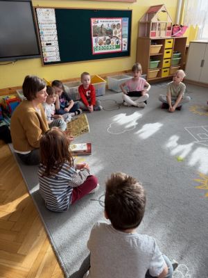 Dzieci siedzą na dywanie i słuchają mamy Stefana która czyta książkę