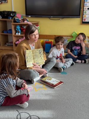 Dzieci siedzą na dywanie i słuchają mamy stefana która czyta książkę