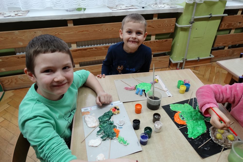 Dwóch chłopców maluje farbami dinozaury z masy solnej