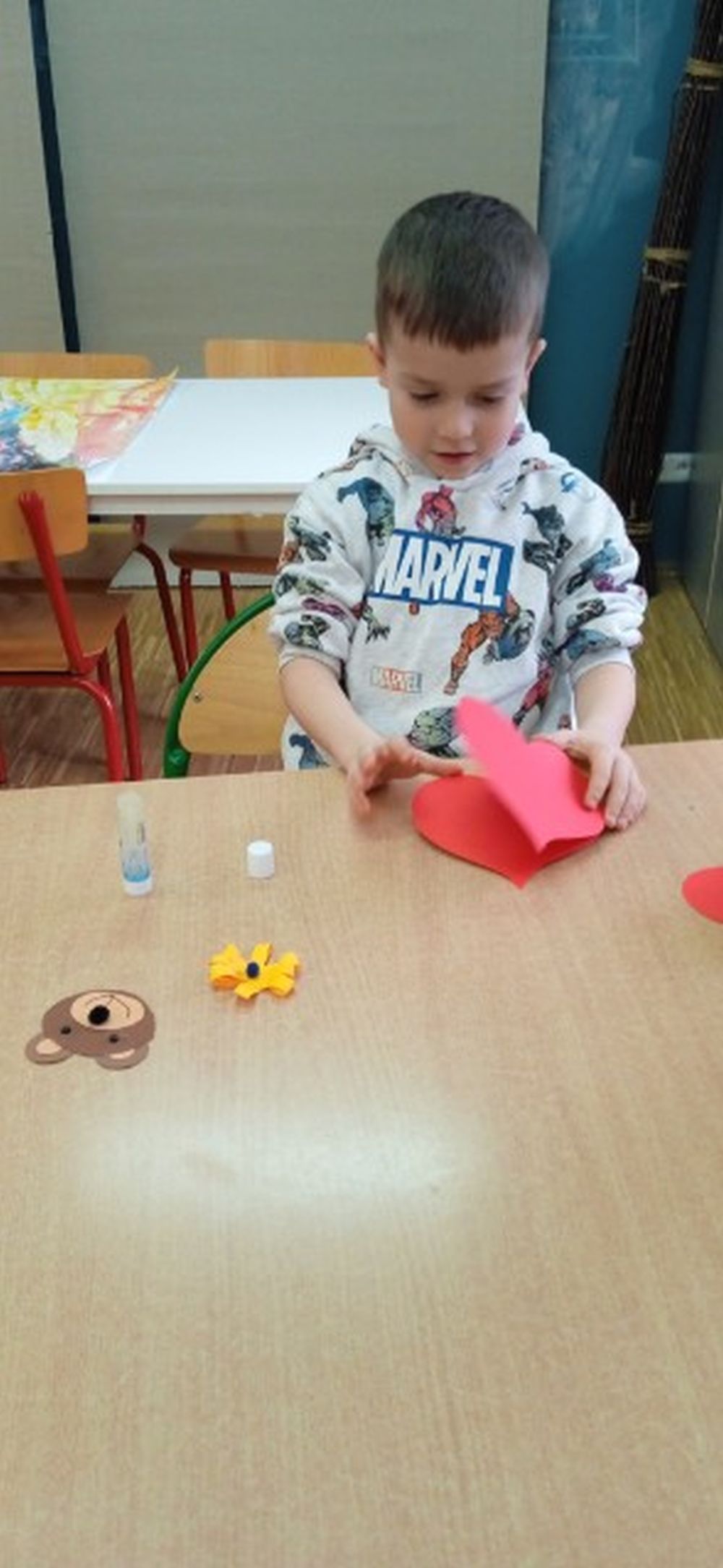 Chłopiec siedzi przy stoliku i robi serduszko z papieru