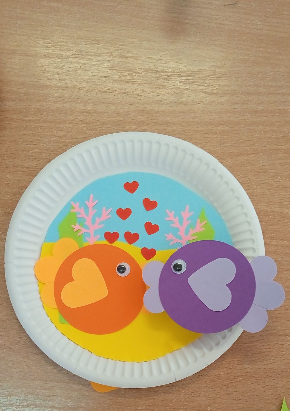 Praca plastyczna na papierowym talerzyku : dno oceanu i dwie kolorowe rybki dające sobie buziaka i serduszka