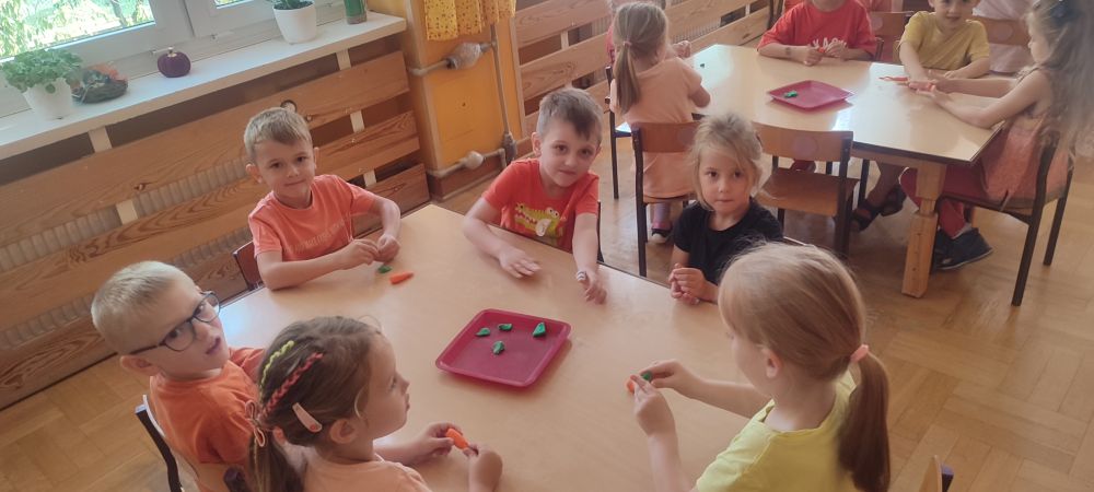 Dzieci siedzą przy stolikach i lepią marchewki z plasteliny