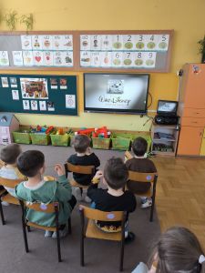 Dzieci siedzą na krzesełkach i oglądają bajkę