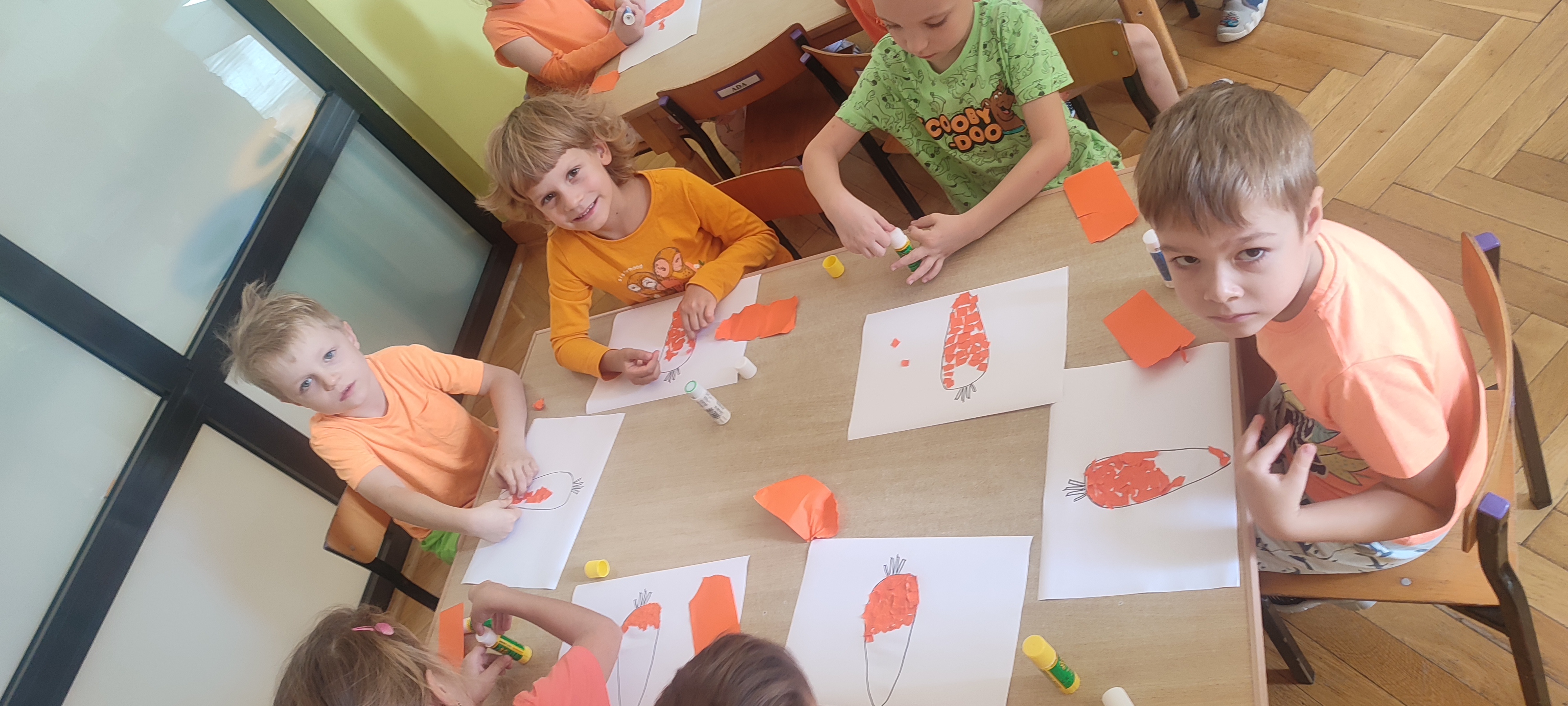 Dzieci siedzą przy stolikach i wykonują pracę plastyczną- marchewka z wydzieranych kawałków papieru