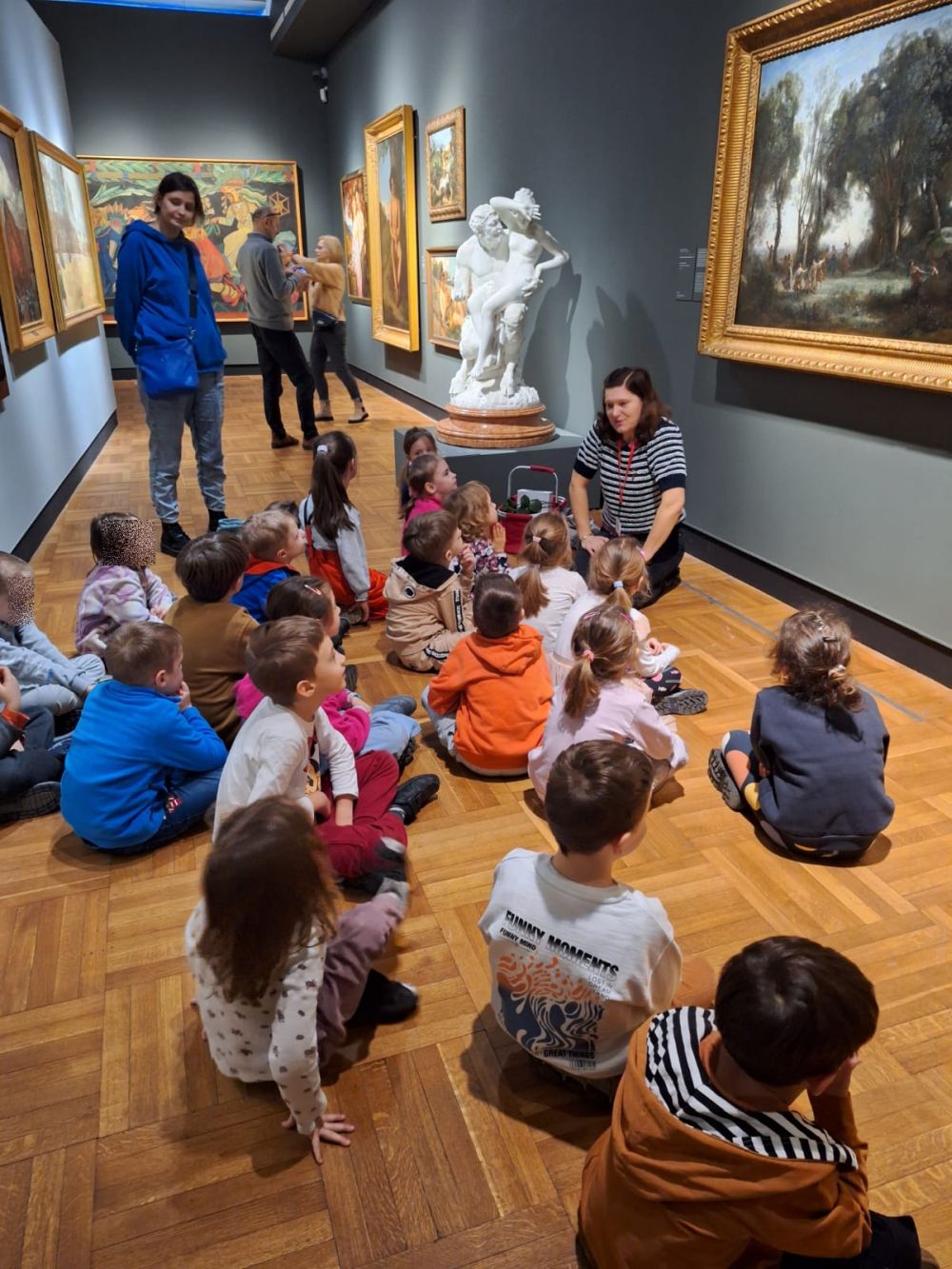 dzieci siedzą w muzeum i patrzą na rzeźby 