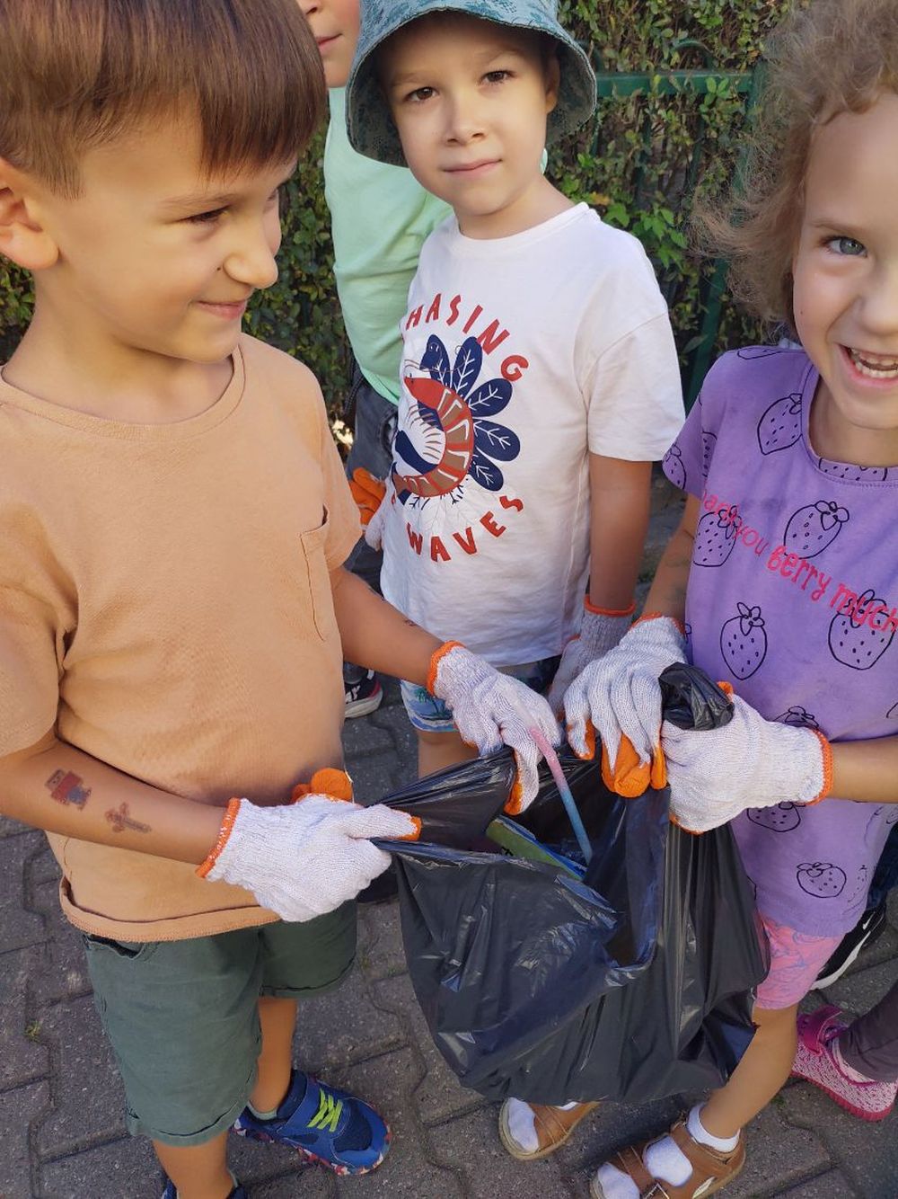 Troje dzieci trzyma worek z zebranymi śmieciami