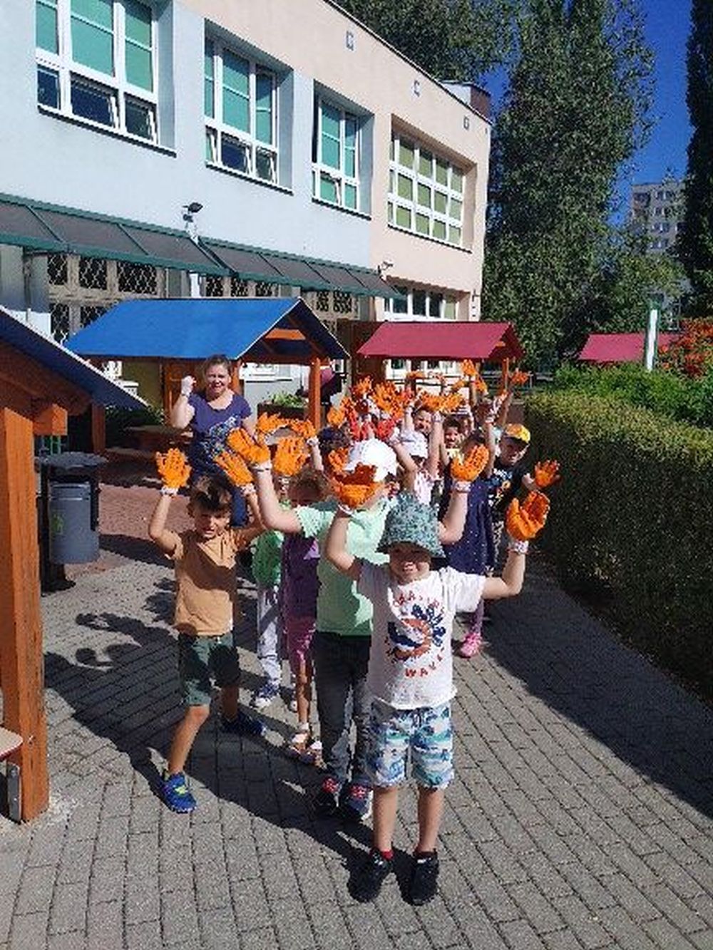 Dzieci z grupy 5 stoją na przedszkolnym placu z rękawiczkami na rękach gotowe do sprzątania świata