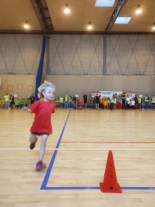 Dziewczynka biegnie na hali sportowej ubrana w strój sportowy 