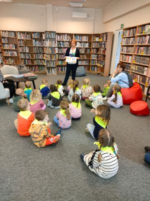 Dzieci siedzą na dywanie i słuchają Pani Bibliotekarki