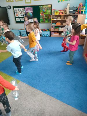 Dzieci maszerują na dywanie trzymając butelki w ręce