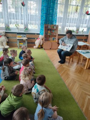 Dzieci siedzą i słuchają bajki czytanej przez rodzica