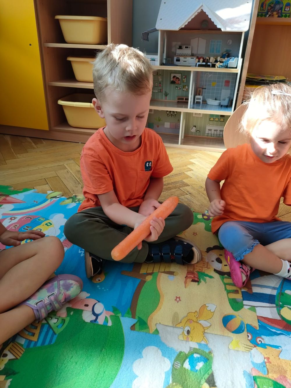 Chłopiec i dziewczynka siedzą na dywanie i podaje sobie marchewkę