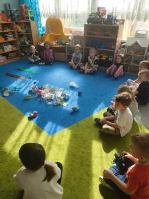Dzieci siedzą na dywanie na środku którego widać rozrzucone śmieci