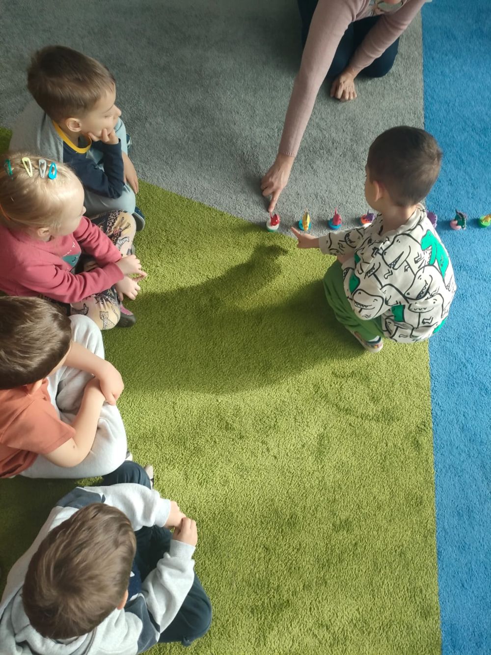 Chłopiec przelicza figurki dinozaurów stojące na dywanie