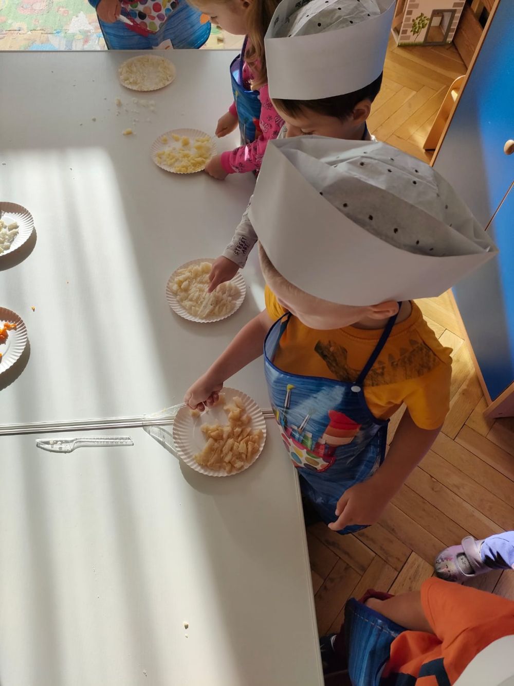 Dzieci w strojach kucharzy kroją warzywa