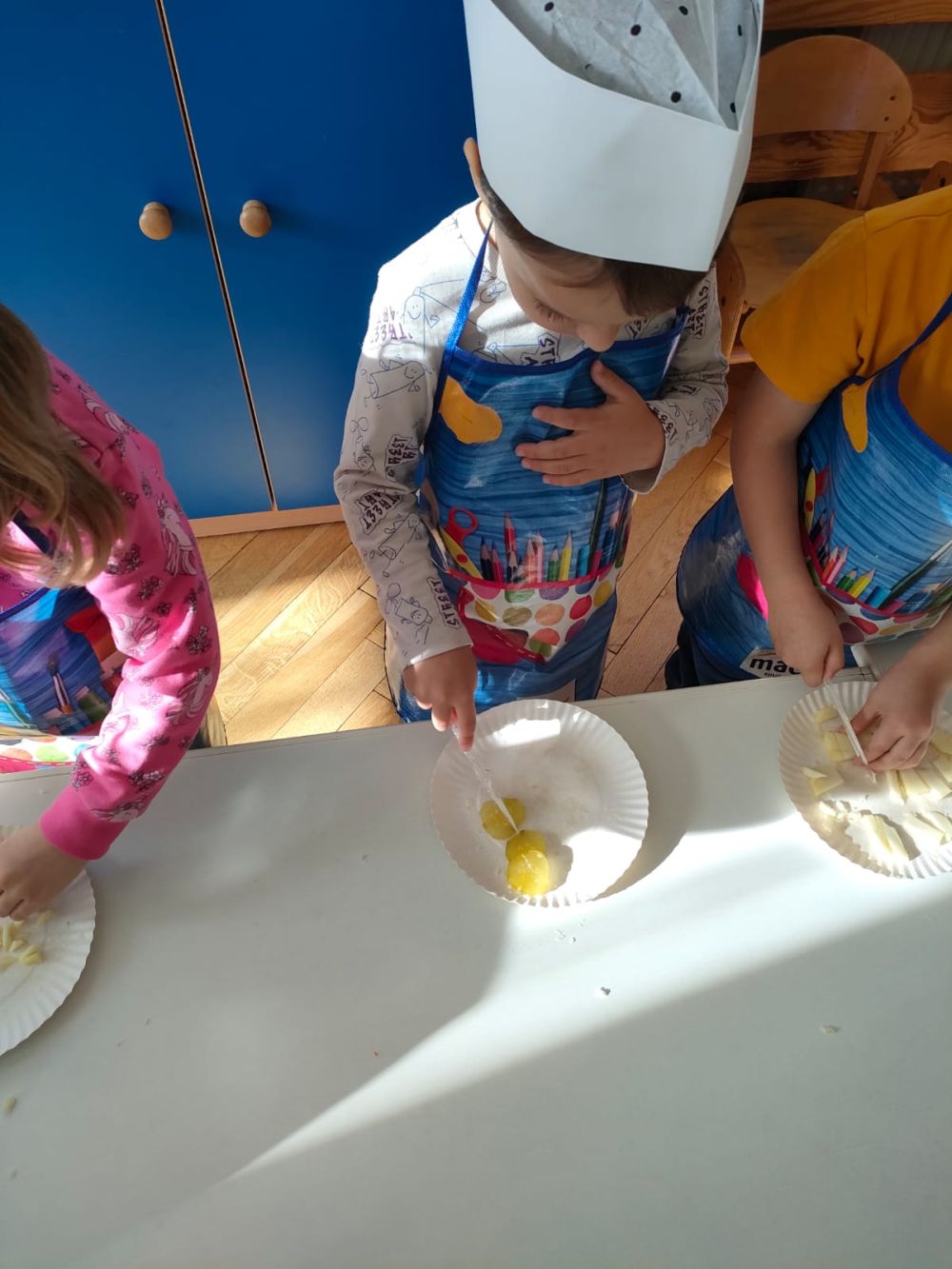 Dzieci w strojach kucharzy kroją warzywa