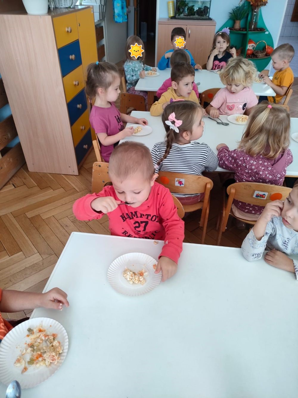 Dzieci siedzą przy stolikach i jedzą sałatkę warzywną