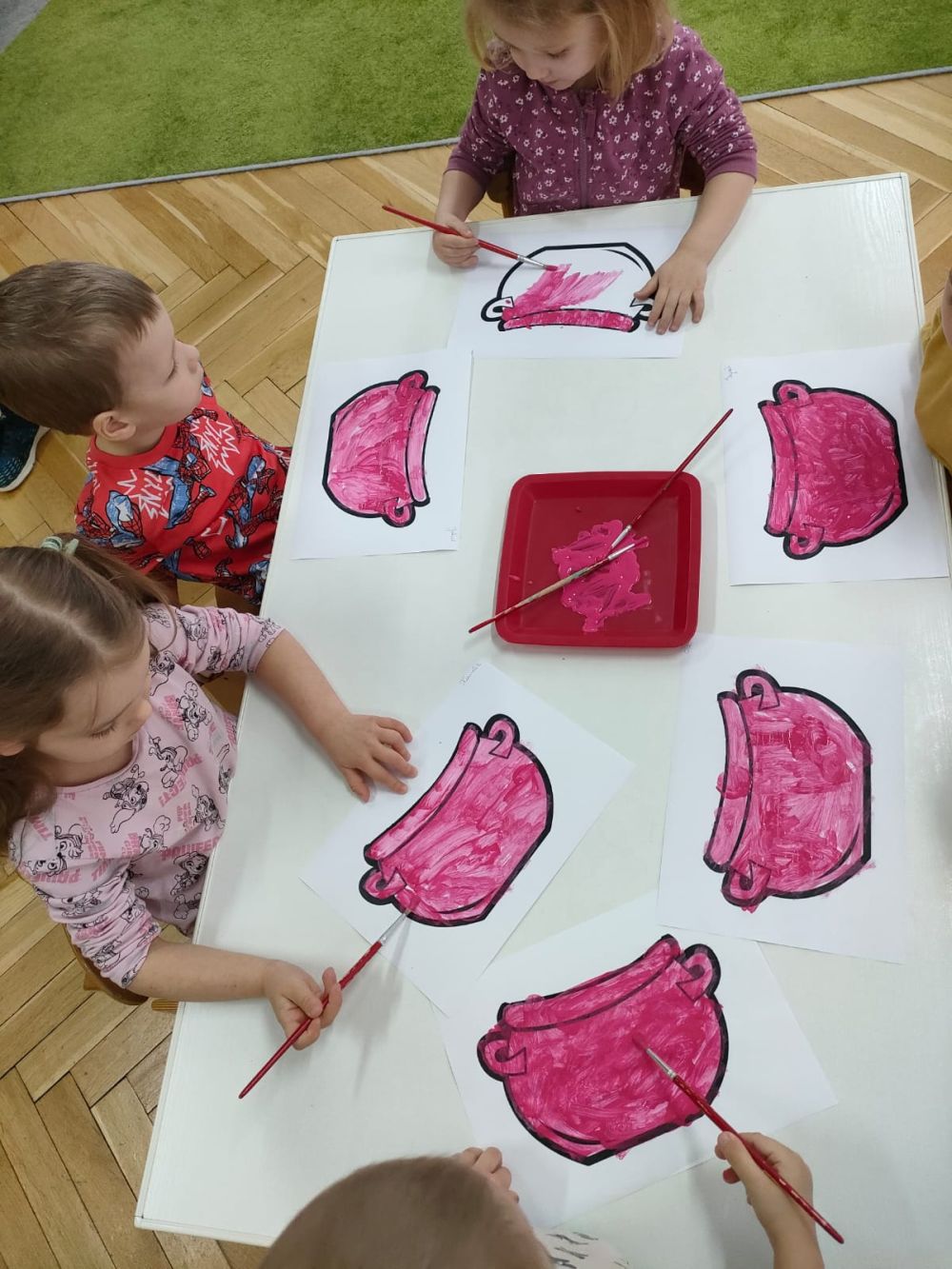 Dzieci malują różową farbą obrazek na którym jest garnek