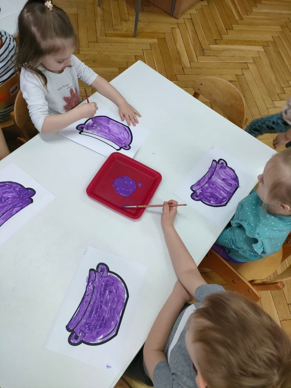Dzieci malują fioletową farbą obrazek na którym jest garnek