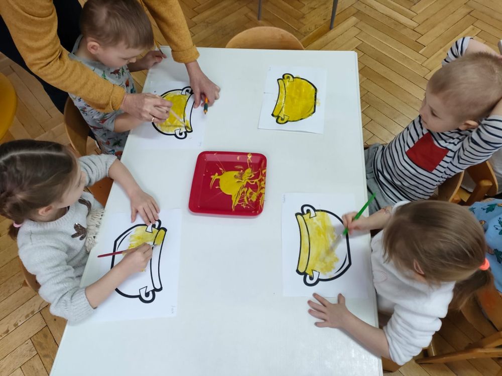 Dzieci malują żółtą farbą obrazek na którym jest garnek