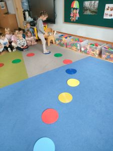 Dziewczynka chodzi po kolorowych dyskach ułożonych w okręgu na dywanie